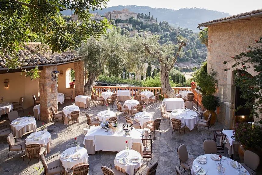 El Olivo's terrace at Belmond La Residencia, set for dinner beneath olive trees with Deià on the hillside behind